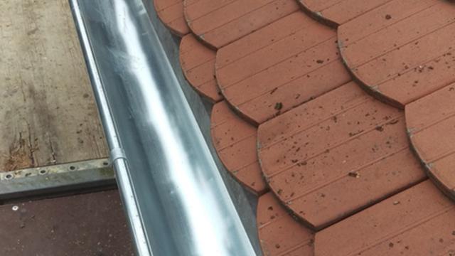 Detailaufnahme einer metallenen Dachrinne auf roten Ziegeln